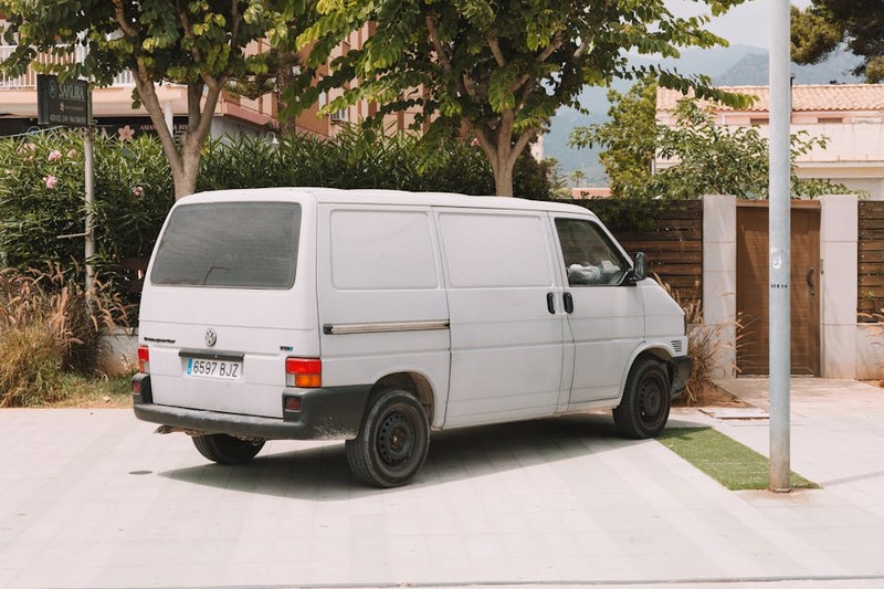 A classic white Volkswagen van parked outdoors in Benidorm, Spain, under the shade of trees.
