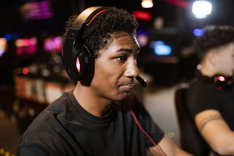 Een moderne draadloze gaming headset met RGB-verlichting en een afneembare microfoon op een bureau met een gamende persoon op de achtergrond.