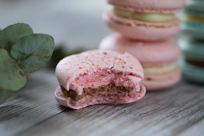 Close-up van een perfect gebakken macaron met glanzende schaal en delicate voetjes, op een pastel achtergrond