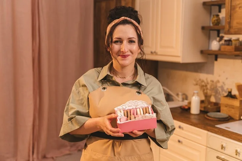 Iemand plaatst voorzichtig macarons in een decoratieve doos, benadrukkend de delicate aard van het gebak